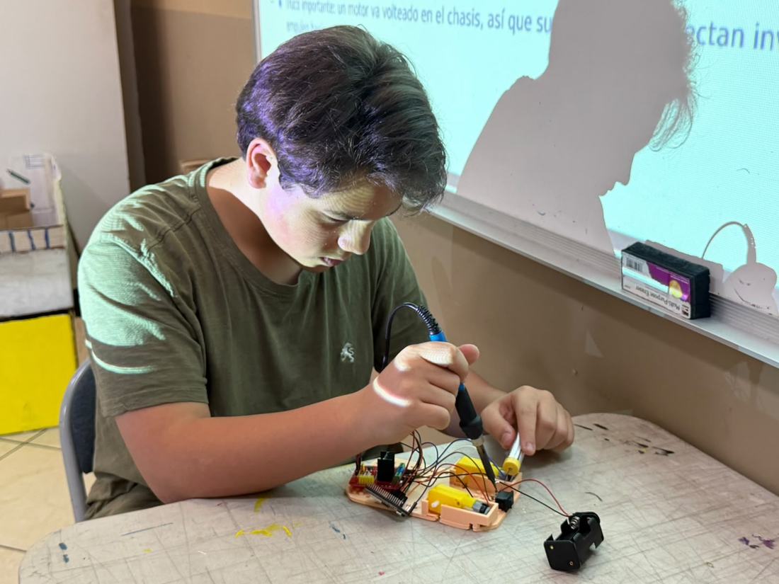 Alumno suelda los cables de un motor sobre el chasis de su robot en un taller de robótica de Qubiko