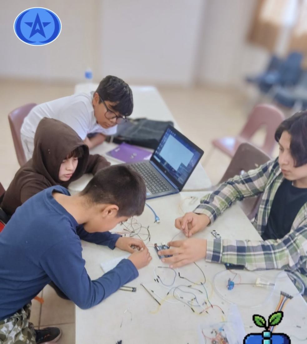 Alumnos armando circuitos alrededor de una mesa con una laptop compartida en un taller de Qubiko