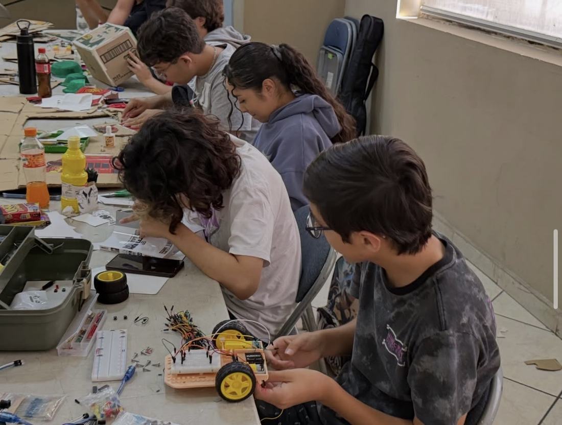 Niños de primaria arman entre todos un carro robot con protoboard, motores y ruedas en un taller de Qubiko