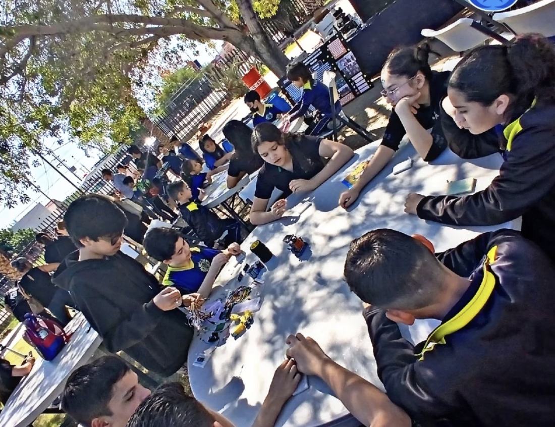 Taller gratuito de robótica de Qubiko al aire libre, con decenas de niños trabajando en mesas bajo los árboles