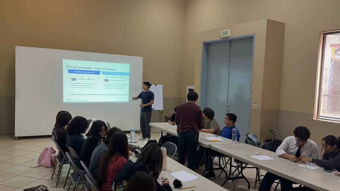 Aula llena de alumnos durante un taller de robótica de Qubiko, con la presentación proyectada al frente