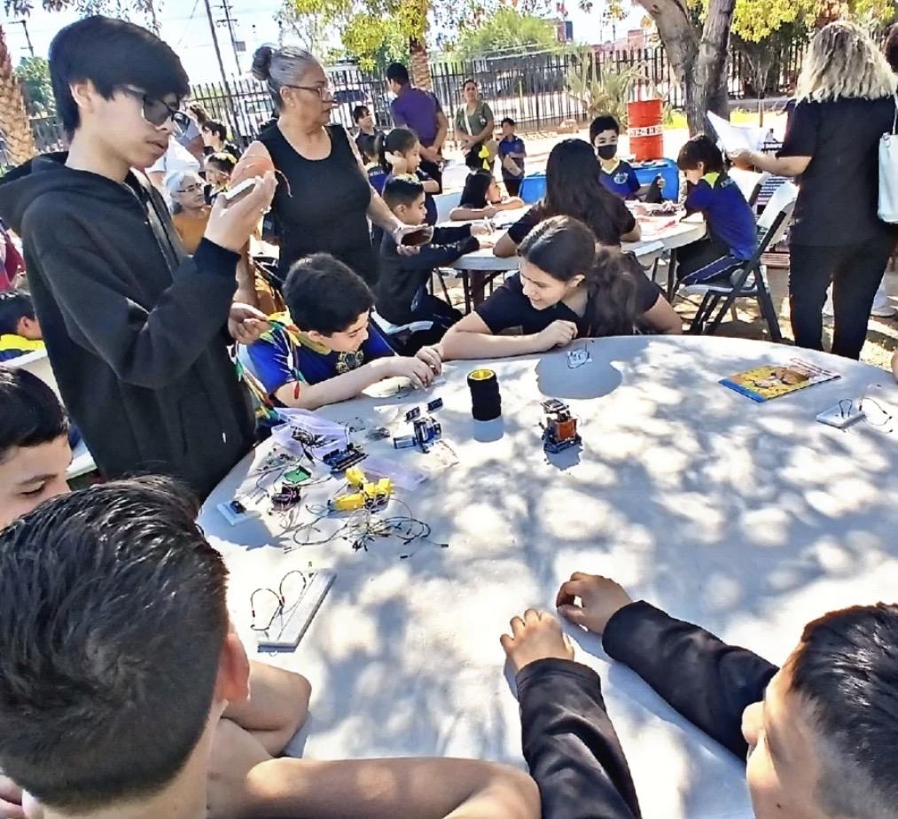 Taller comunitario de robótica de Qubiko en un parque, con niños armando circuitos sobre una mesa redonda