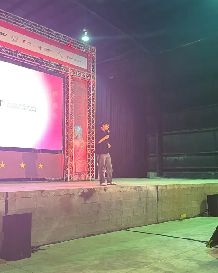 Presentación de Qubiko con micrófono en el escenario de CREO MX Rosarito, junto a la pantalla del evento